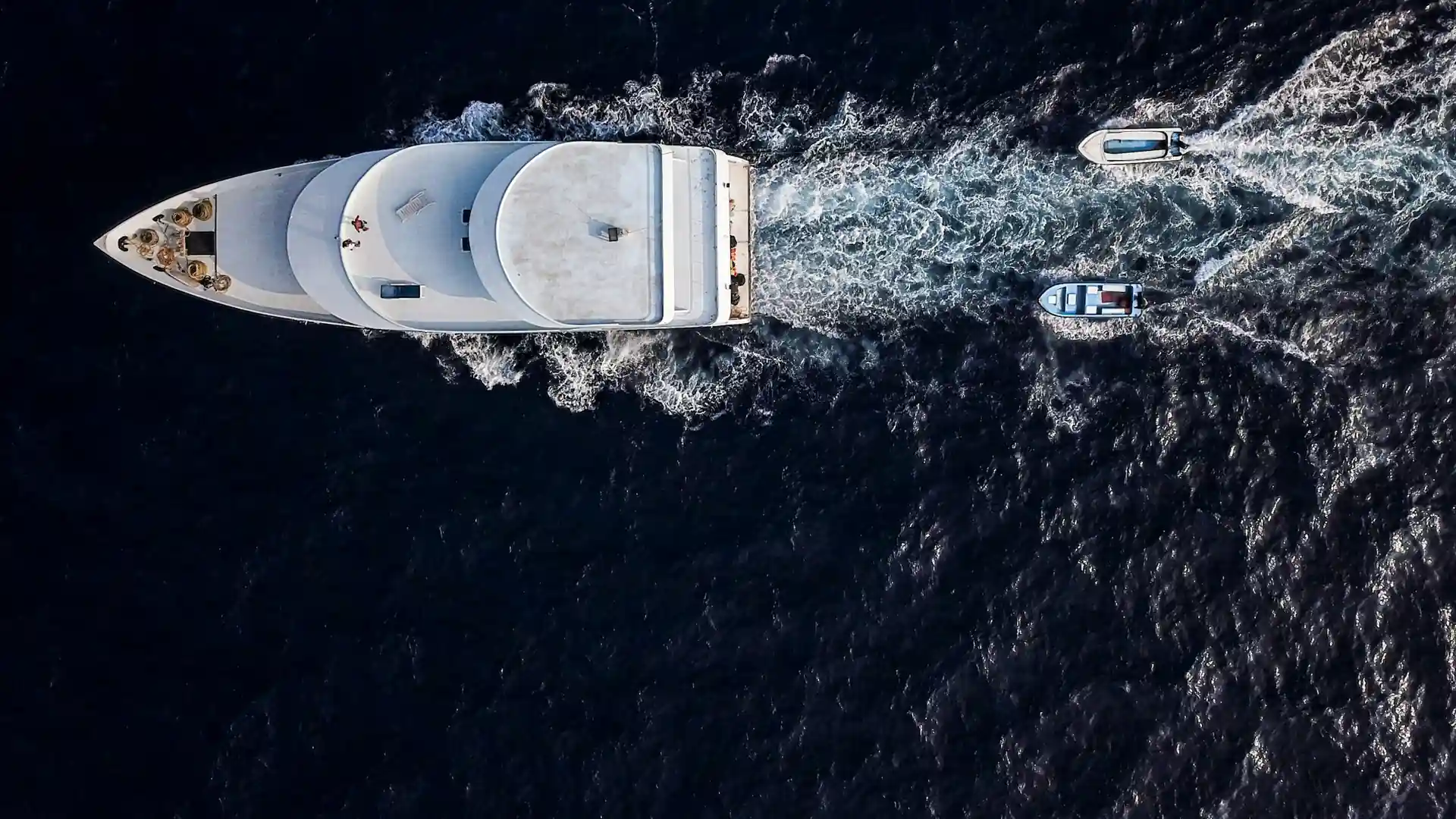 Aerial view of a superyacht and its tenders crossing dark open water
