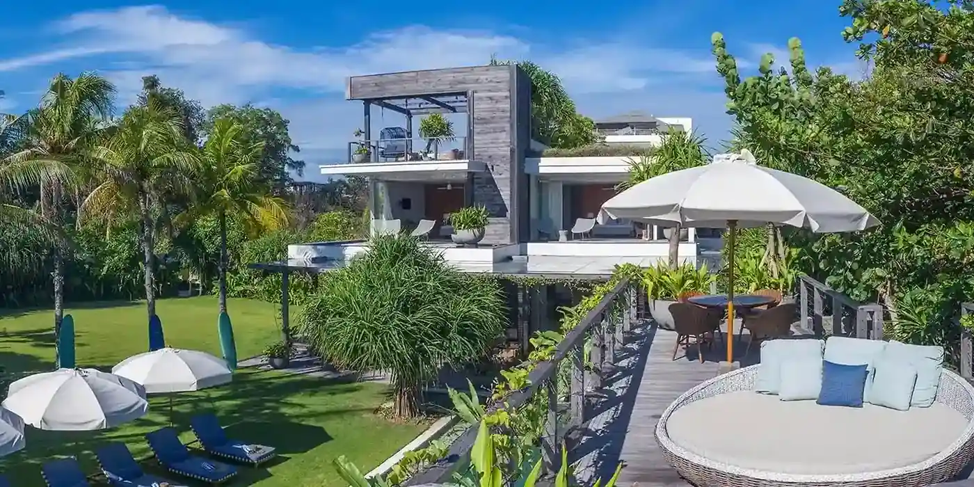 Beachfront villa with a palm-lined lawn, white umbrellas and a timber deck daybed