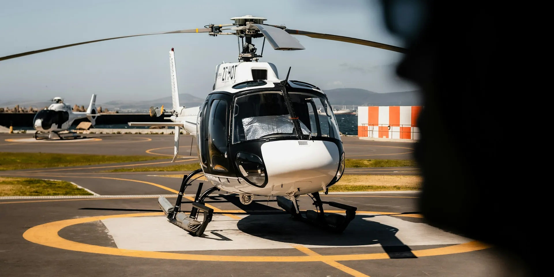 White helicopter parked on a helipad, a second helicopter behind it