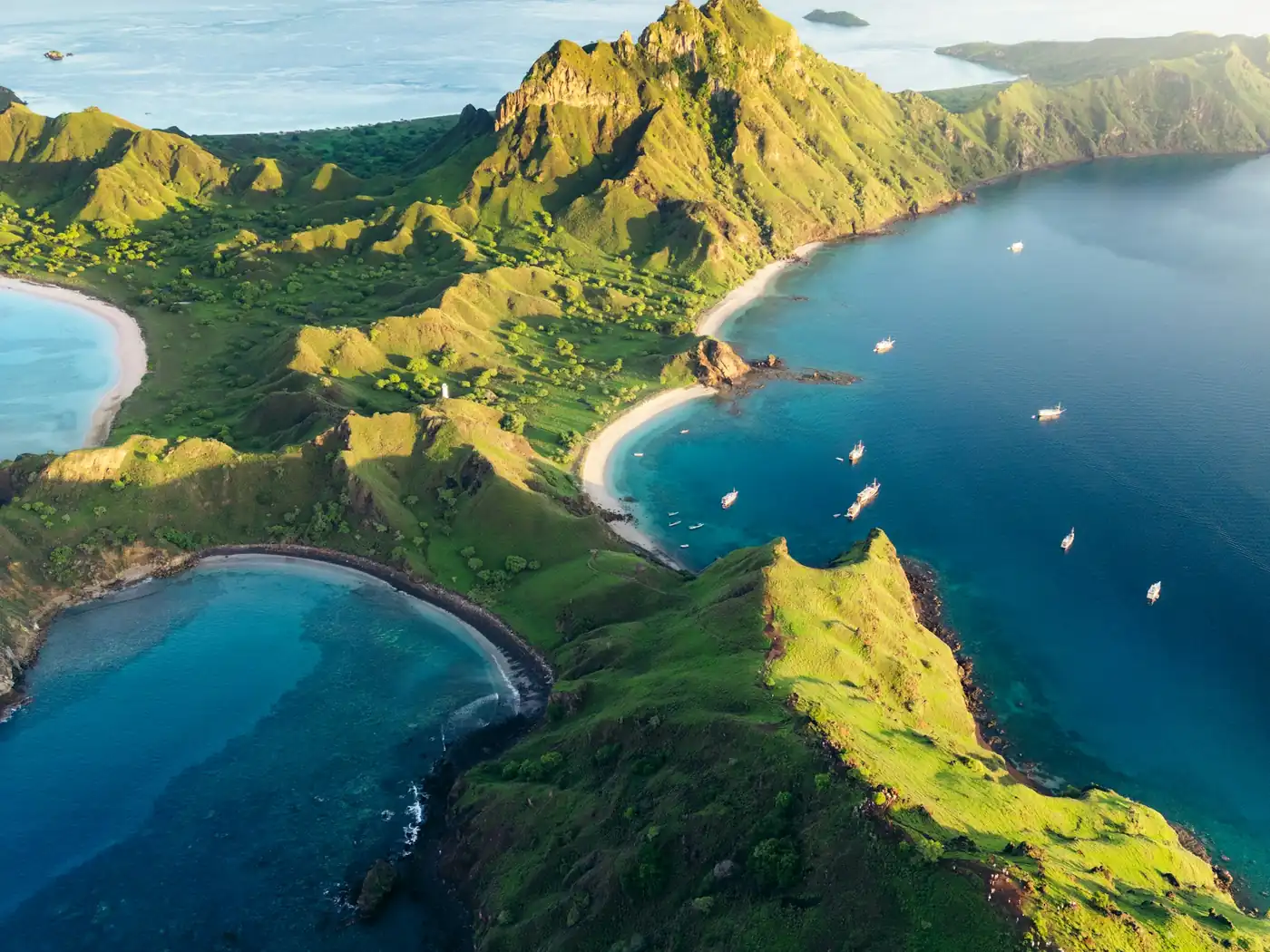 Aerial view of Padar Island’s green ridges and curved bays, with boats anchored offshore in Komodo